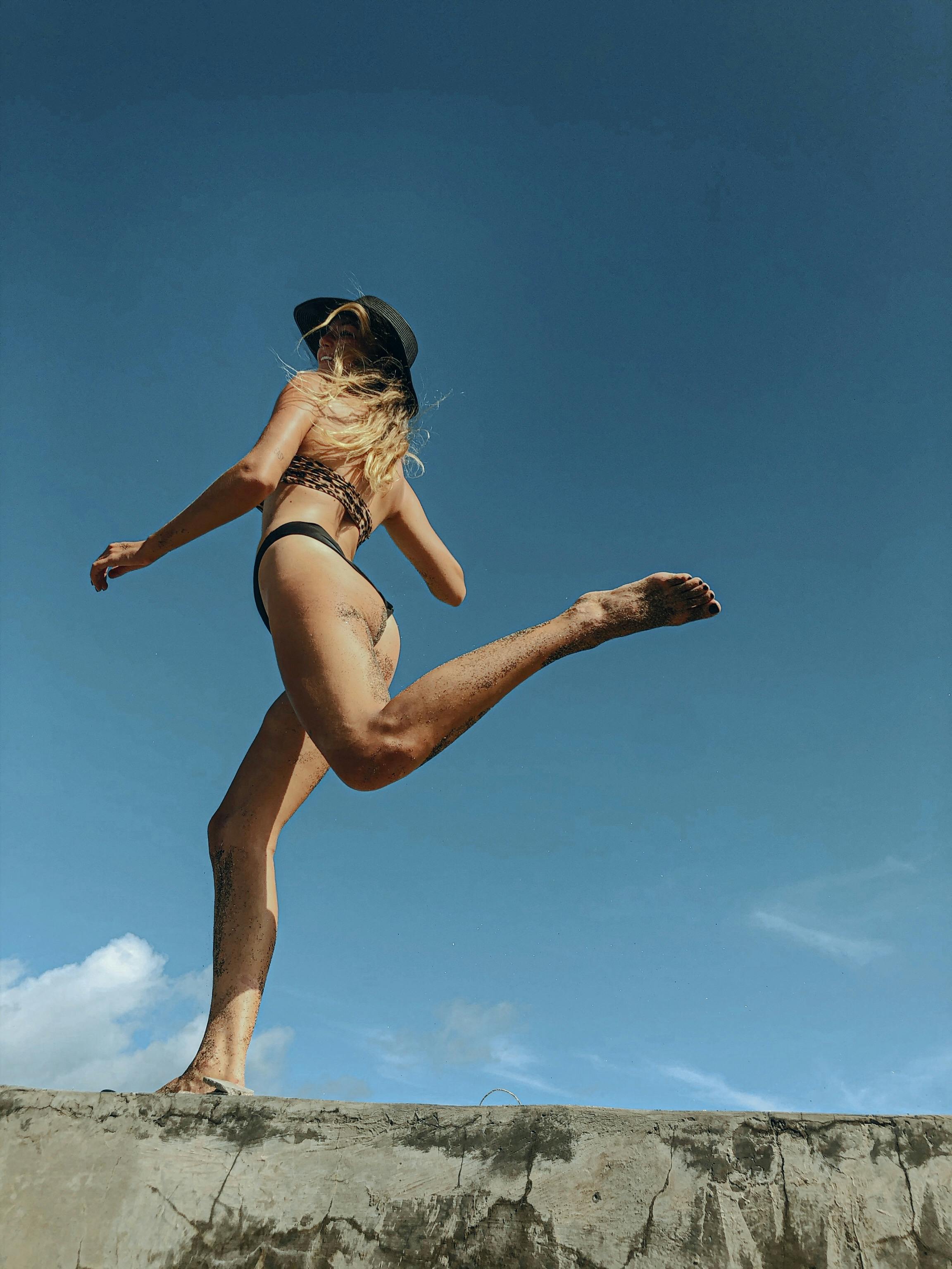Free Woman in a bikini leaping under a clear blue sky, exuding summer vibes. Stock Photo