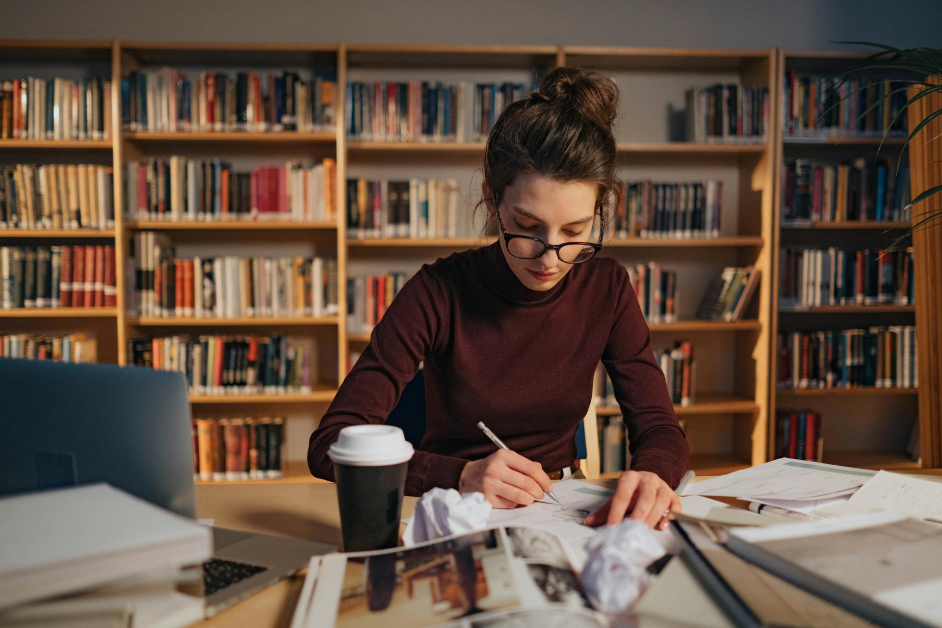 Female student concentrating on creative work in a library environment.