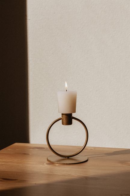 Elegant minimalistic candle in a brass holder casting shadows on wooden table.