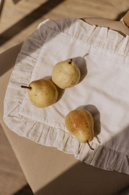 Three ripe pears placed on a rustic, ruffled cloth with soft natural lighting.