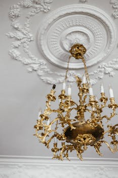 A luxurious gold chandelier suspended from an intricately designed white ceiling.