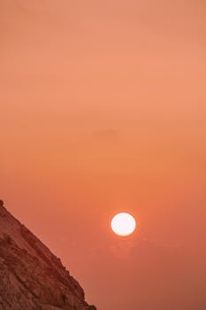 A calming view of the sun setting over a rocky landscape with warm orange hues.