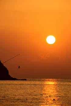 Peaceful sunset over the ocean with silhouette of a fishing pole casting into the water.