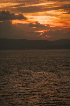 Capture of a tranquil ocean at sunset with dramatic clouds and vibrant orange sky.