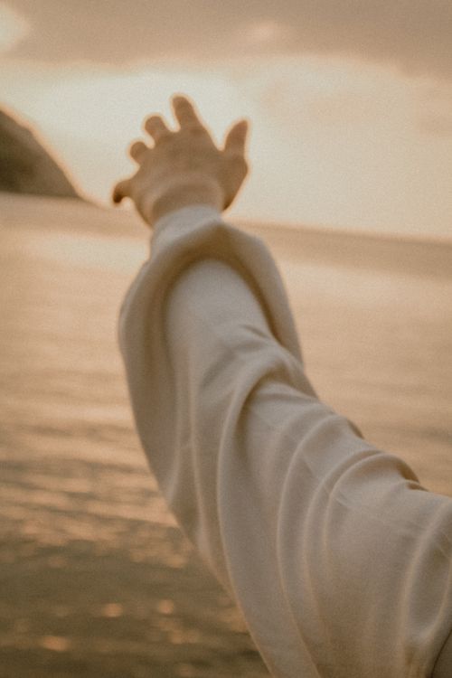 Free A sepia-toned image of an outstretched arm reaching towards the serene horizon over the sea. Stock Photo