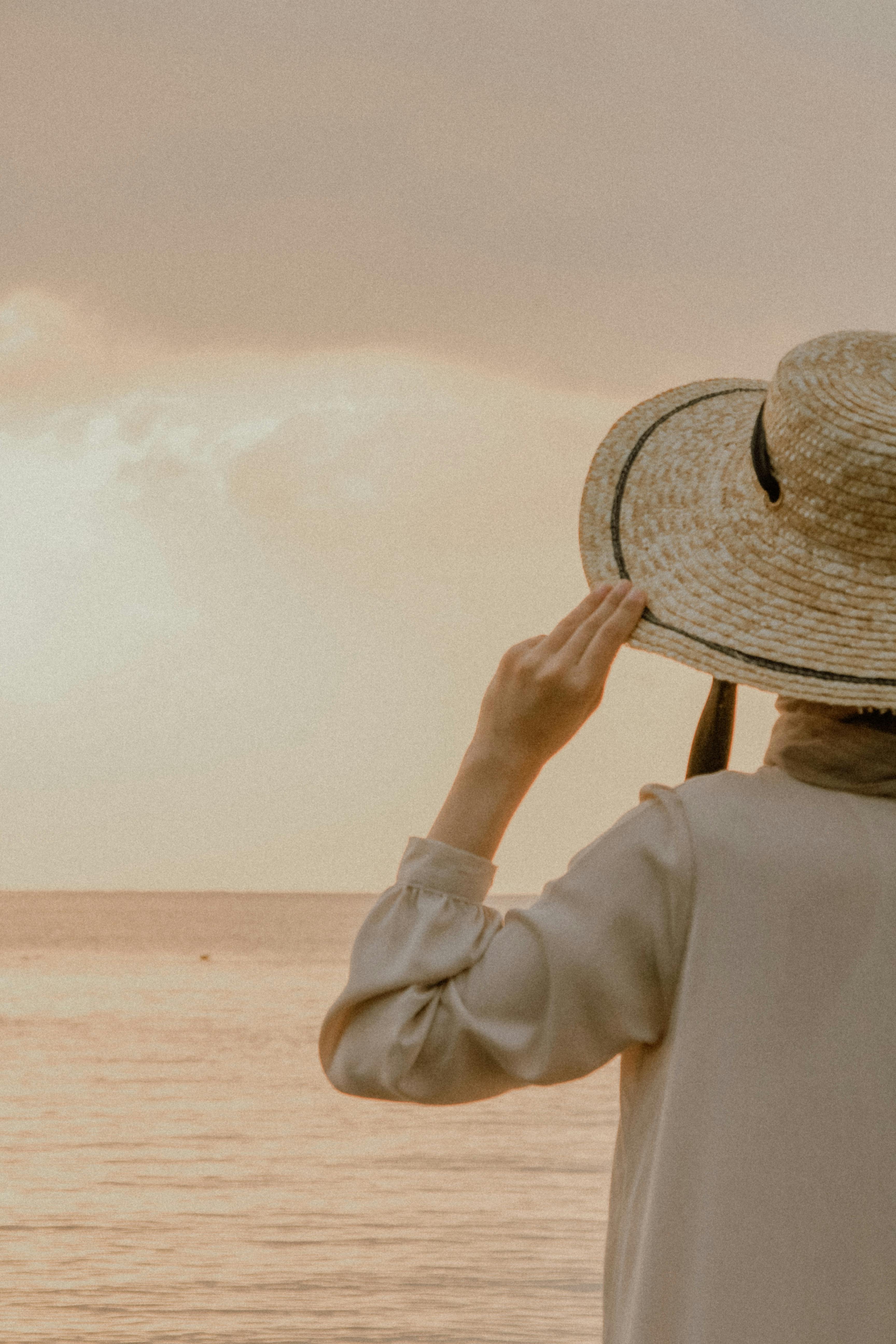 身穿米色连衣裙、戴草帽的女子欣赏日落时分宁静的海景
