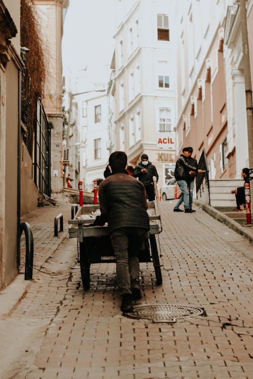 Free Man Pushing a Cart Along the Small Street Made of Bricks Stock Photo