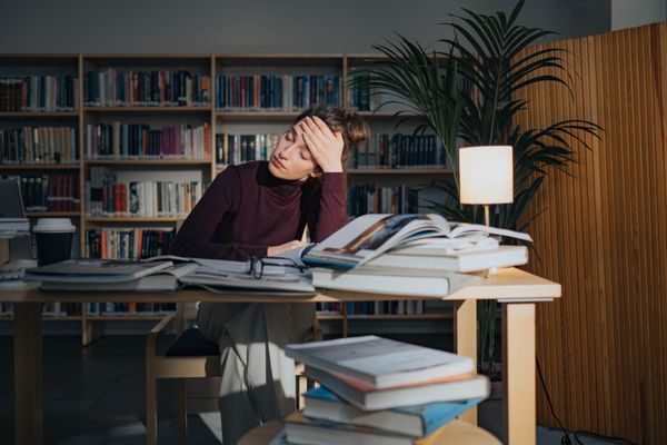 Mujer agotada rodeada de libros estudiando