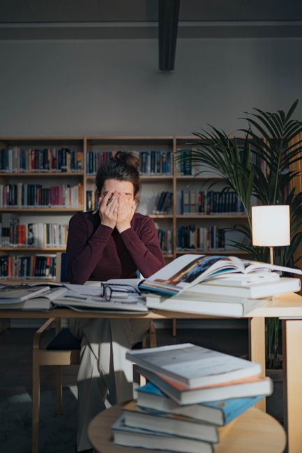A stressed woman surrounded by books and papers, studying late in a library