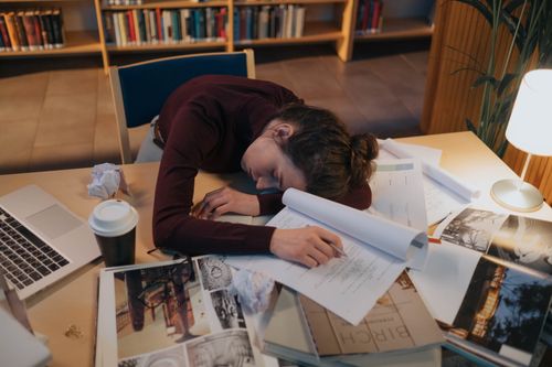 Free A tired woman asleep at a desk with papers in a library setting, illustrating overwork. Stock Photo