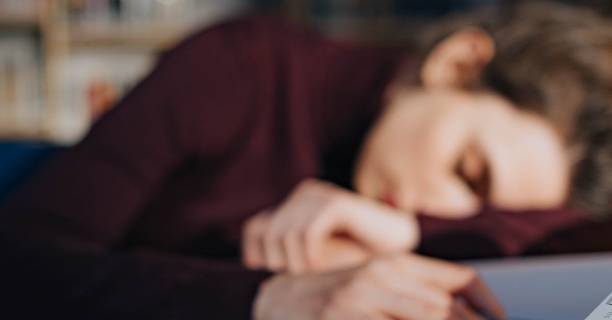 A tired student sleeping on a table surrounded by books, paper, and eyeglasses.