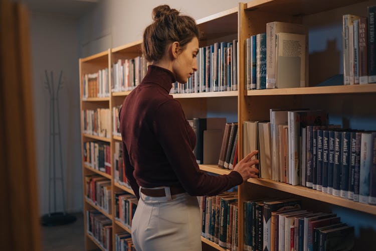 Woman Searching For A Book From The Bookshleves