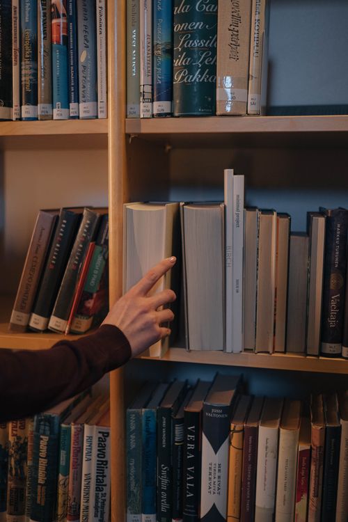 Free A hand reaches for a book on a neatly organized wooden bookshelf. Stock Photo