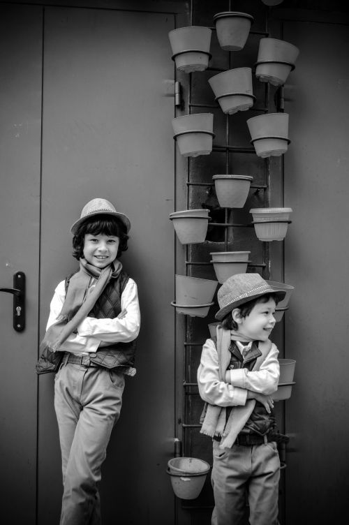 Free Two children in hats and scarves posing by stacked pots in a monochrome setting. Stock Photo