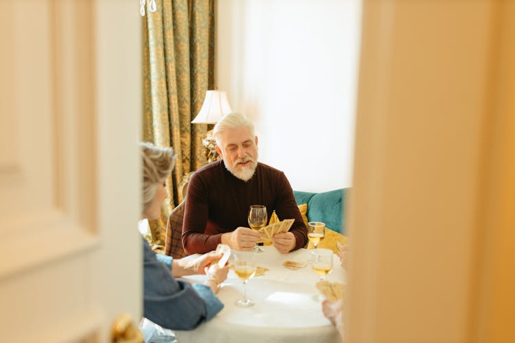 An Old Man In Brown Sweater Sitting On Chair While Playing Cards