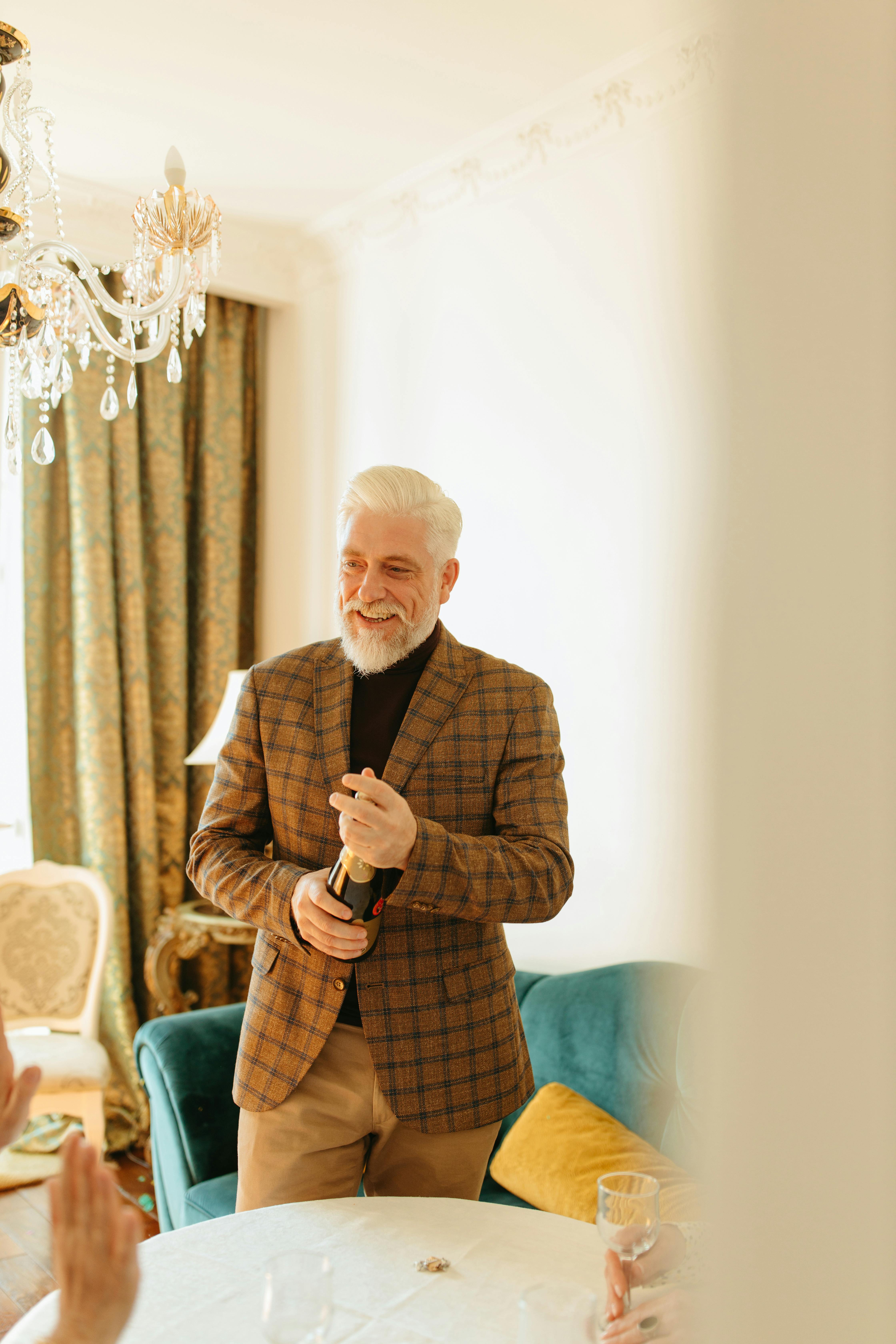 Smiling senior man opening a bottle of champagne in an elegant room, capturing a moment of celebration.