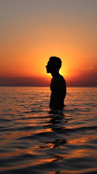 Striking silhouette of a man in the sea against a vibrant sunset sky in Türkiye.