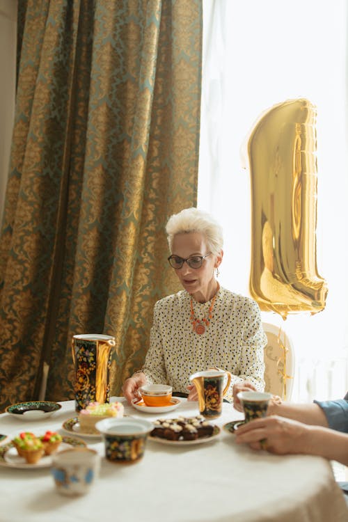 Elderly Woman Sitting at the Table with a Birthday Balloon behind Her 