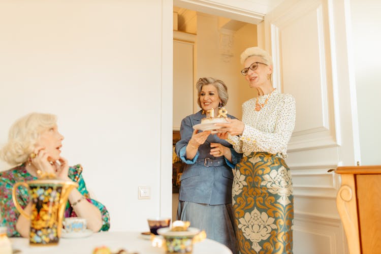 An Elderly Women Holding A Cake While Greeting Their Friend