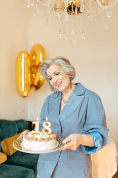 Happy senior woman with stylish gray hair holding an 18th birthday cake indoors.