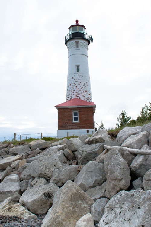 Free A classic lighthouse standing on a rugged coastline with a rocky foreground. Stock Photo
