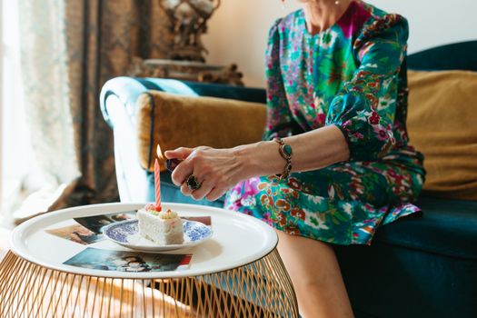 Elegant elderly woman lighting a candle on a cake, wearing a vibrant floral dress indoors.