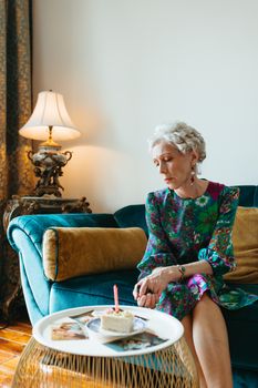 Senior woman reminiscing with old photos in a cozy living room, capturing memories.