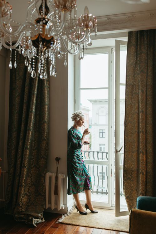 Free Senior woman in elegant attire smoking by a bright window indoors. Stock Photo