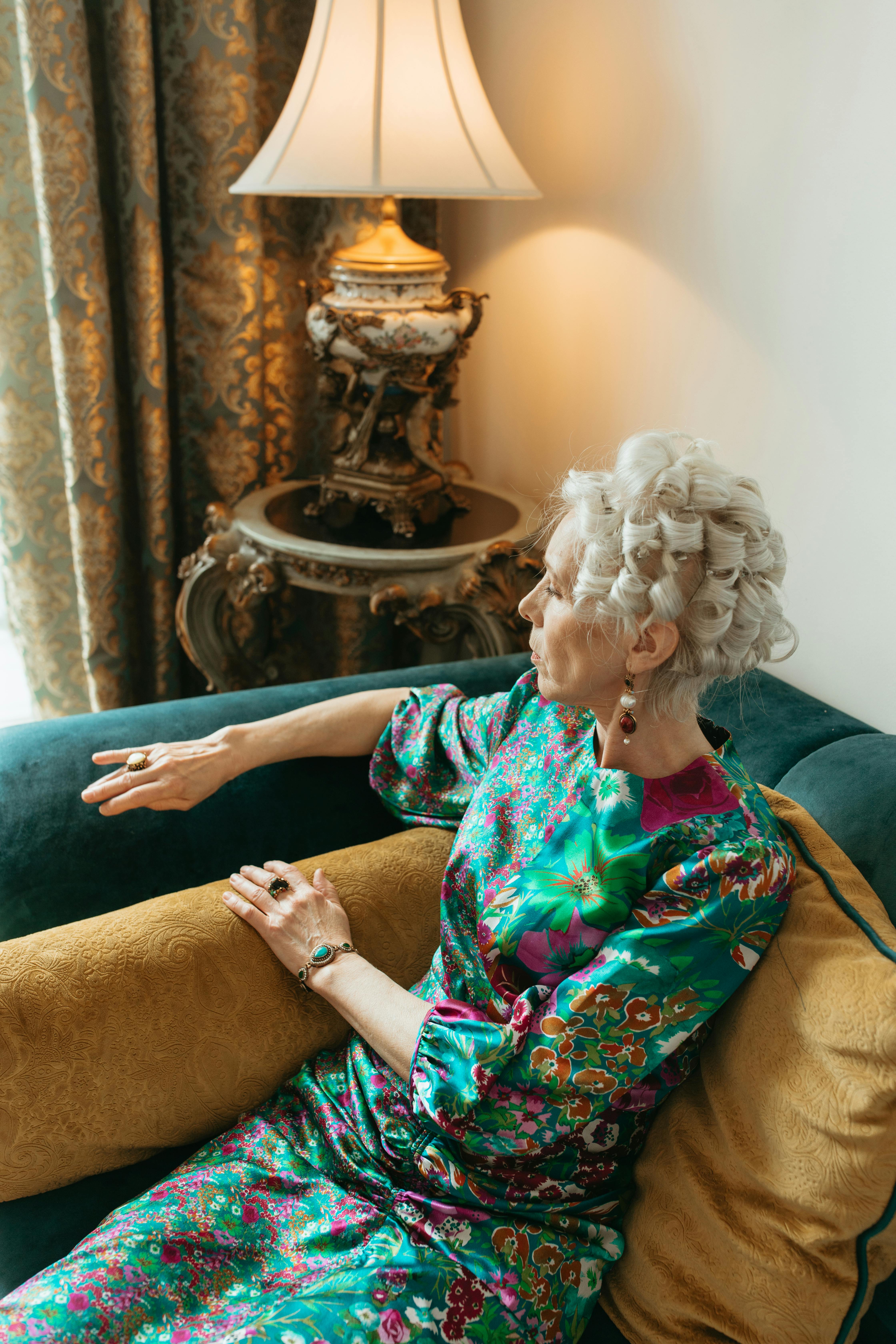Senior woman in floral dress sitting on vintage sofa, exuding elegance and tranquility.