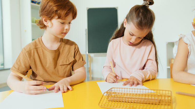 Dua anak menulis bersama di meja kelas
