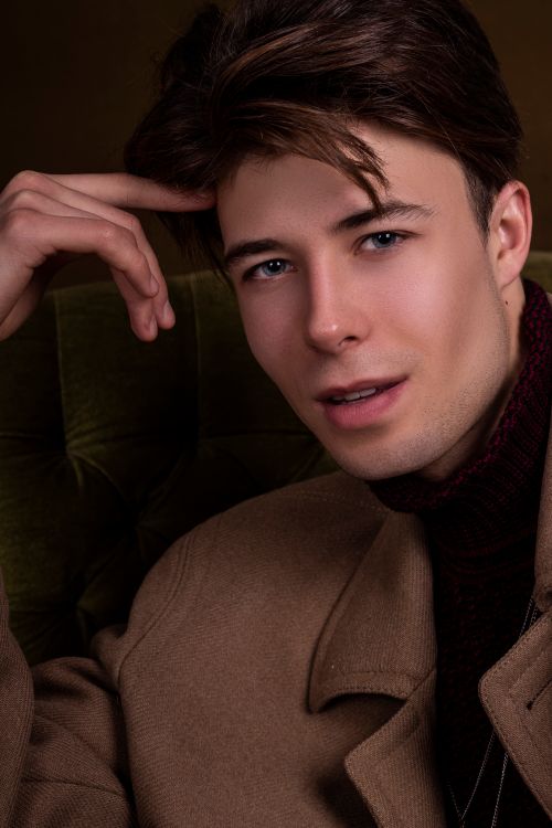 Free Close-up portrait of a handsome young man with styled hair in a tan coat indoors. Stock Photo
