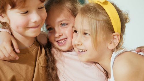 Free Three cheerful children share an embrace, smiling brightly in a warm setting. Stock Photo