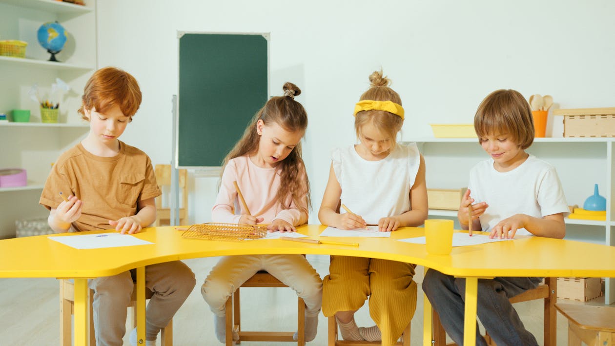 Free Kids Sitting on Yellow Table Writing  Stock Photo