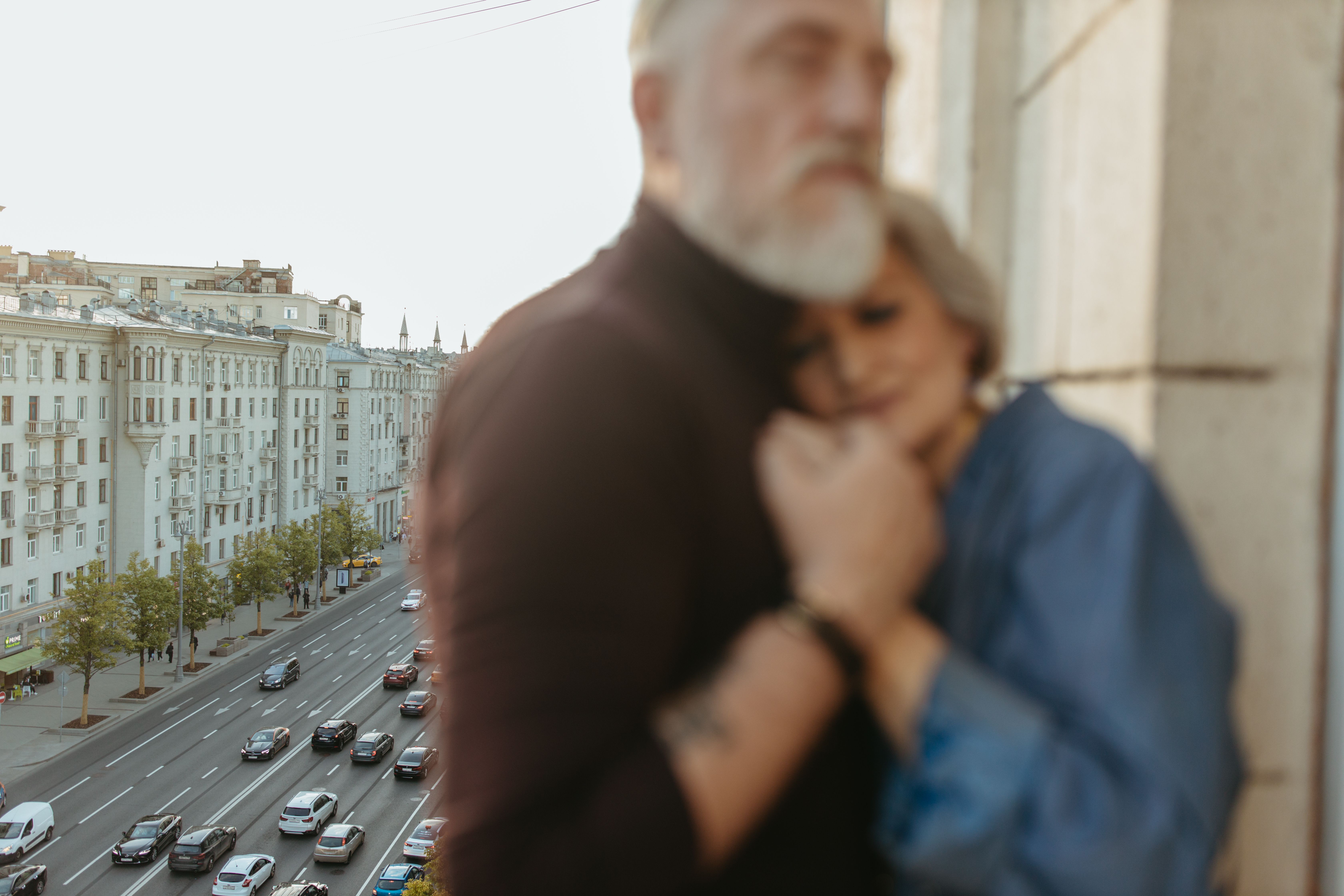 Blurred couple embracing on a balcony overlooking a busy city road.