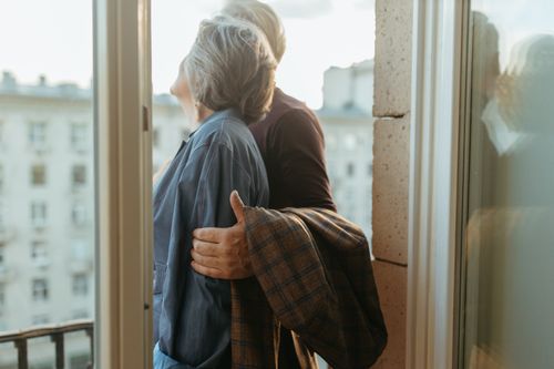 Free An elderly couple lovingly embracing while standing on a city balcony. Stock Photo