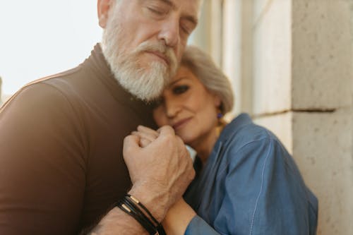 Close-Up Photo of an Elderly Couple Standing Close to Each Other while Holding Each Other's Hands
