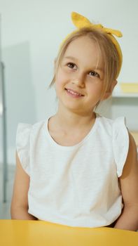 Portrait of a cheerful young girl wearing a yellow headband with a white top.