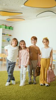 Four cheerful children standing together, smiling in a classroom environment with bright decor.
