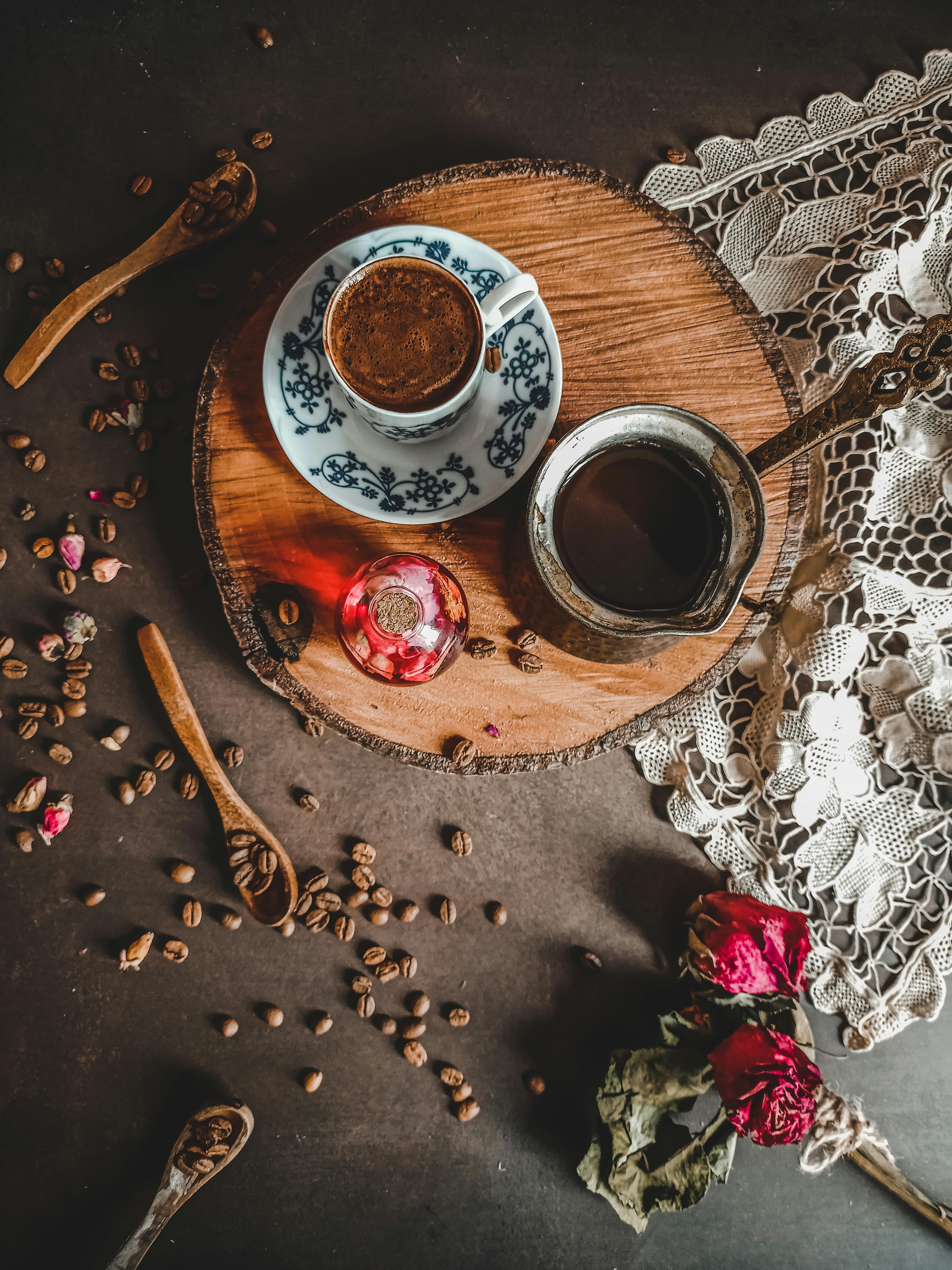 Artistic flat lay of espresso with rustic elements, lace, and dried roses, perfect for a cozy ambiance.
