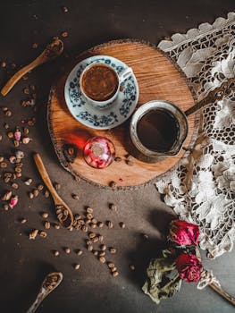 Artistic flat lay of espresso with rustic elements, lace, and dried roses, perfect for a cozy ambiance.