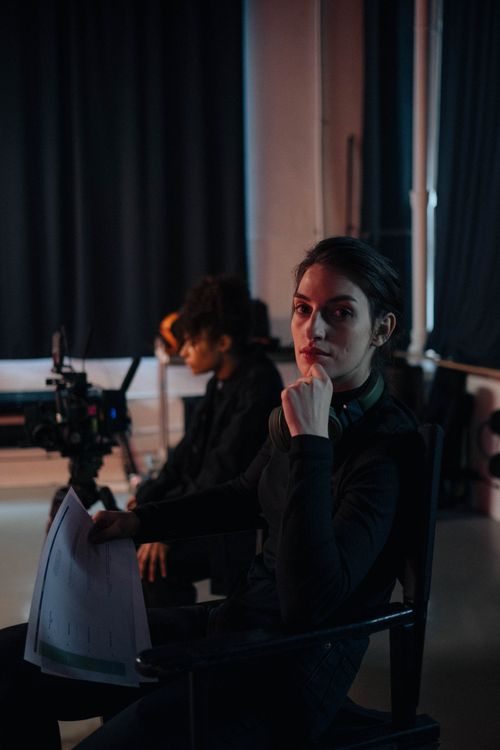 Free A focused female director sits holding a script on a film set, emphasizing creativity and teamwork. Stock Photo