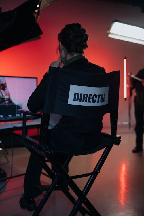 A Person Sitting on Directors Chair Near a TV Screen