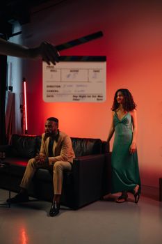 Two actors on a film set with dramatic lighting and a clapboard.