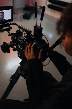 Close-up of a videographer adjusting a camera on a tripod in a studio setting.