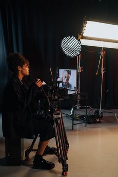 Videographer operating camera in a dark studio with lighting equipment and monitors.