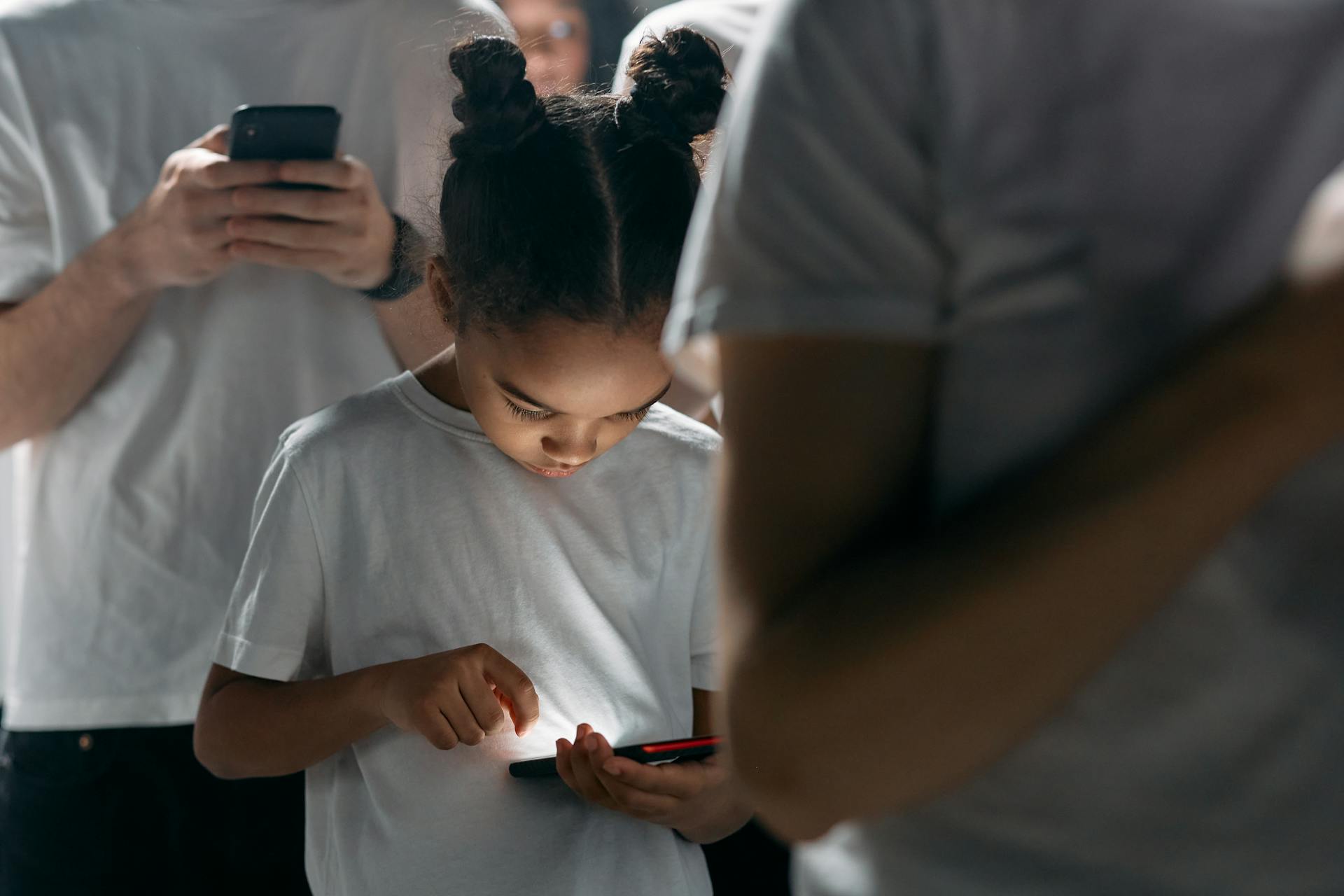 A young girl engrossed in her smartphone amidst a group of people using mobile devices indoors.