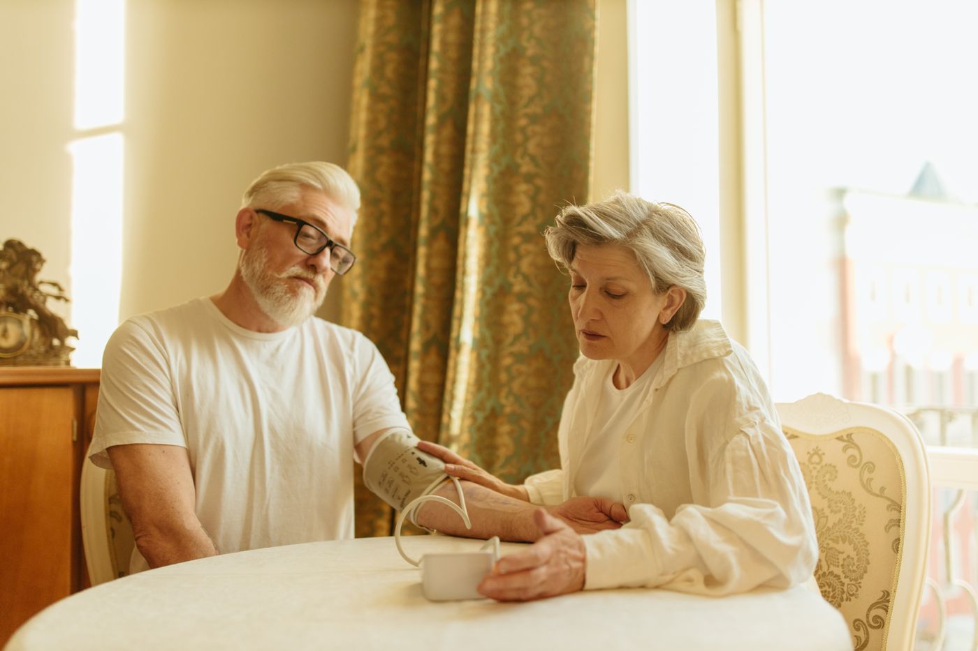Older couple using a digital blood pressure monitor together in a bright home wellness setting