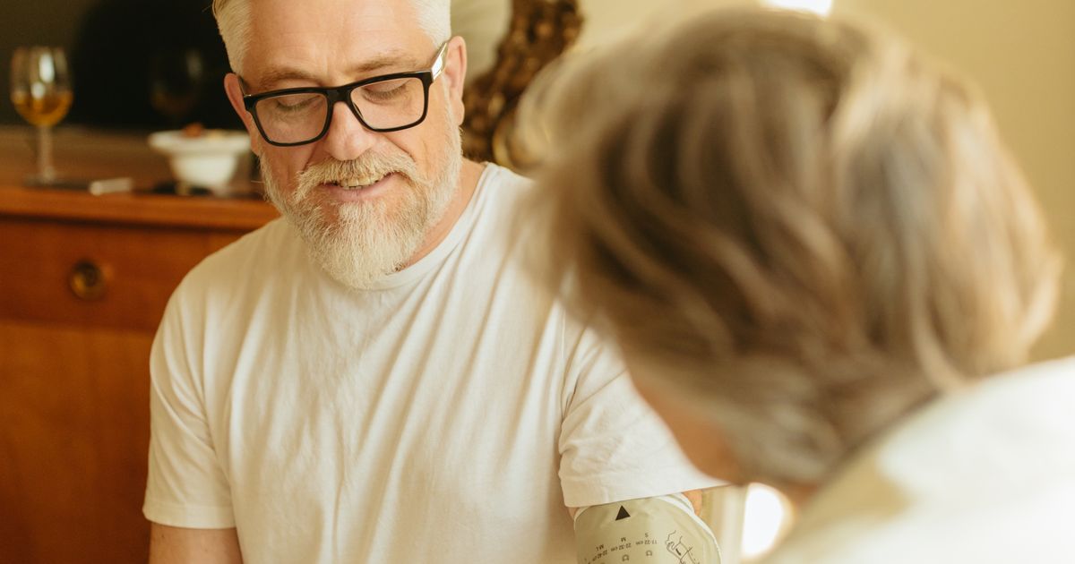 Senior man with gray hair and glasses checking blood pressure using a digital monitor at home