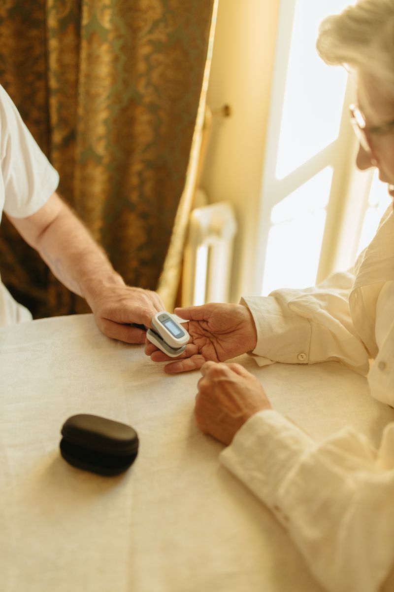 A care worker placing a pulse oximeter on a resident's finger at a table by a window