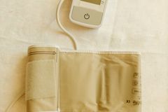 Top view of a digital blood pressure monitor and cuff on white fabric background.
